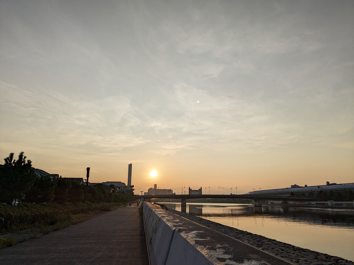 川沿いの防波堤がある道。遠くに朝日が昇ってきているのが見える。
